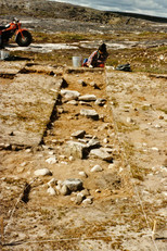 Site IcGm-4, area A, Annie Weetaluuktuk examines a trench in the excavation zone (facing north), 1986