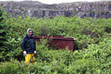 Willie Kumarluk debout devant une grosse bassine utilisée pour faire bouillir la graisse de baleine sur le site du poste de Petite rivière de la Baleine (GlGe-9) (photo de Christian Roy)