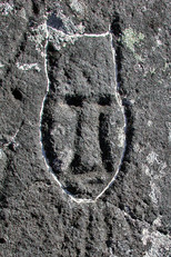 Petroglyph of an elongated figure with a prominent forehead ending in narrow points along each side of the face; the base of the figure is oval in shape. The carvings beneath the chin may symbolize shamanic breathwork. The whitened edges indicate relatively recent “updating” work on the carving, 2004